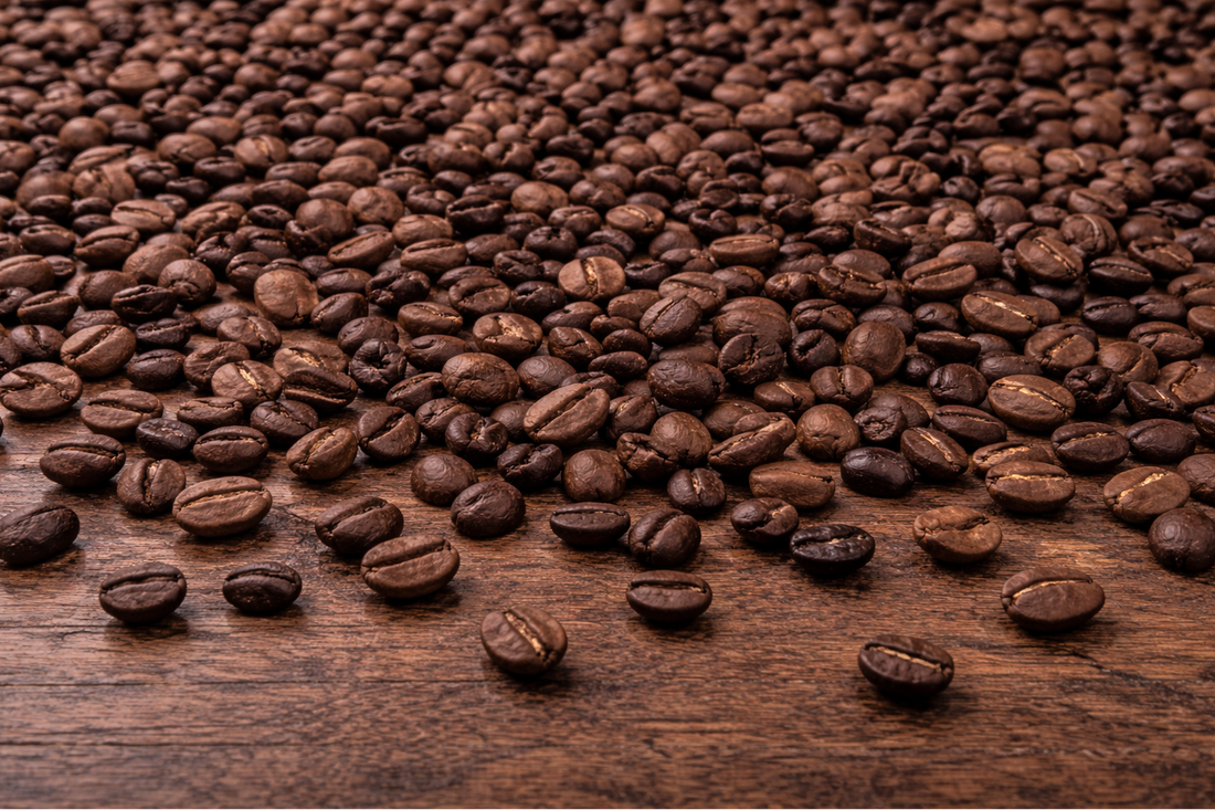Roasted coffee bean blend on wooden table with mostly Arabica and some darker Robusta